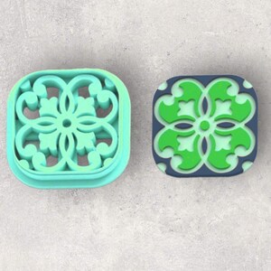 May include: Two square cookie cutters, one is light blue with a white and green intricate design, the other is dark blue with a green floral design.