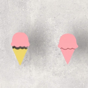 Könnte beinhalten: Zwei Eiswaffel-förmige Dekorationen. Eine hat eine rosa Kugel mit einer schwarzen und gelben Waffel. Die andere ist eine einfarbige rosa Eiswaffel. Der Hintergrund ist eine hellgraue, strukturierte Oberfläche.