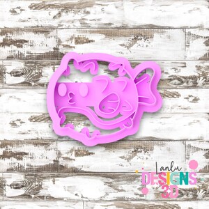May include: A bright pink plastic cookie cutter shaped like a pufferfish with detailed embossed facial features including round eyes, a small mouth, and fins. The design features a rounded body with spikes along the edges and a tail on the right side.