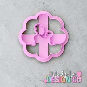 May include: A pink cookie cutter shaped like a flower with a cross design. The cross features parent and child silhouettes. The text "Wendy Lu DESIGN co" is at the bottom.