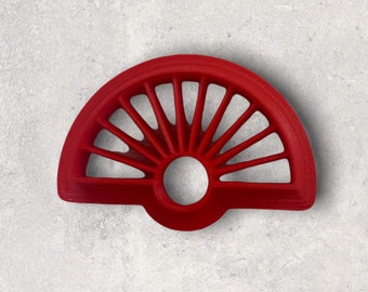 May include: A bright red, semi-circular cookie cutter with a sunburst design. The cutter features a series of straight lines radiating from a central circular opening, creating a fan-like pattern. The cutter is made of a solid material.