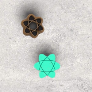 May include: Two star-shaped cookie cutters. One is brown and features an open design with intersecting lines. The other is a bright teal color with a solid outline and a geometric pattern inside. Both are on a gray surface.