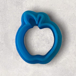 May include: A bright blue apple-shaped cookie cutter. The cutter is made of plastic and has a detailed outline of an apple, including the stem and the indentation at the bottom. The cutter is designed for baking and crafting.