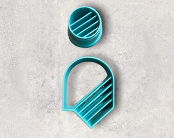 Può includere: Due formine per biscotti in plastica turchese. Una è un cerchio con linee diagonali, l'altra è un rettangolo arrotondato con linee diagonali. Le formine sono su una superficie grigia.