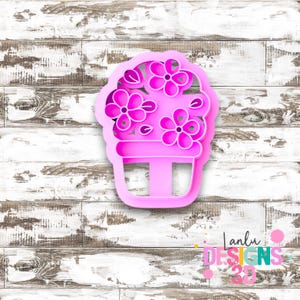 May include: A bright pink cookie cutter shaped like a potted plant with three distinct flowers blooming from the top. The design features a rounded pot base and five-petaled floral shapes, creating a clear outline for baking or crafting projects.
