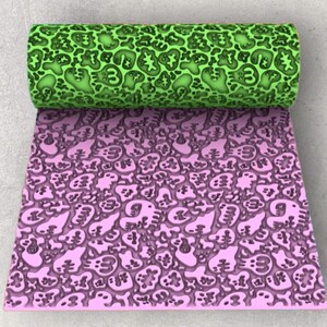 May include: A rolled green sheet with a repeating pattern of abstract shapes and the number 3 sits above a flat pink sheet with the same design. The sheets are likely made of a flexible material, possibly for crafts.