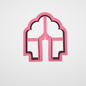 May include: A pink cookie cutter shaped like an arched window or doorway. The cutter features a detailed design with a rounded top and rectangular base, ideal for baking themed biscuits.
