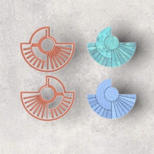 May include: Four decorative geometric shapes in shades of orange, teal, and blue. Each shape features a semi-circular design with radiating lines and a central circle. The shapes are arranged on a light gray surface.