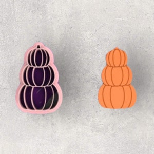 Könnte beinhalten: Ein rosa Plastik-Ausstecher in Form eines Stapels von vier Kürbissen. Daneben liegt ein Stapel von vier orangefarbenen Kürbissen.