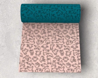 May include: A roll of teal fabric with a repeating pattern of white cats. The fabric is unrolled to reveal a pink fabric with the same cat pattern in a darker shade of gray.