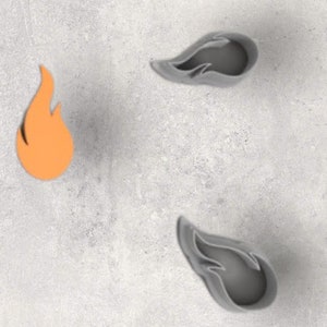 May include: An orange flame-shaped cutout and three grey flame-shaped moulds are arranged on a light grey surface. The cutout is a solid orange colour, while the moulds have a three-dimensional appearance with a darker grey interior.