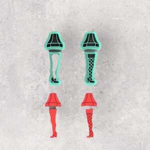 May include: Four shoe charms shaped like lamps with leg bases. Two charms are teal with black details, one featuring a plain leg and one with a fishnet pattern. Two charms are red with black details, one with a plain leg and one with a fishnet pattern.