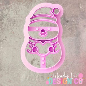 May include: A pink snowman-shaped cookie cutter with a hat, scarf, and heart-shaped design. The cutter has a detailed outline, including facial features and buttons. The design is perfect for holiday baking.