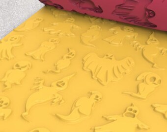 May include: A yellow rolling pin with embossed ghost shapes, partially rolled out on a yellow surface. The unrolled portion of the pin is a deep pink color, also with ghost designs. The design is for Halloween-themed baking.