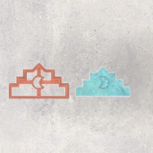 Peut inclure: Deux emporte-pièces. L'un est un contour cuivré d'un motif en gradins avec une découpe en croissant de lune. L'autre est une version turquoise unie de la même forme avec un motif de croissant de lune.