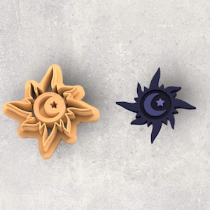 May include: Two cookie cutters, one tan and one dark blue, each featuring a sunburst design with a crescent moon and star. The tan cutter is a layered design, while the blue one is a solid color.