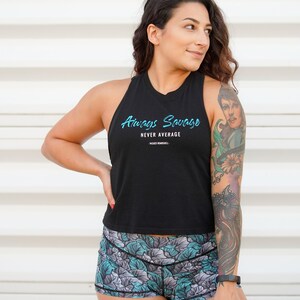 May include: A woman wearing a black tank top with the text "Always Savage Never Average" and floral print athletic shorts. She has a colorful tattoo on her arm.