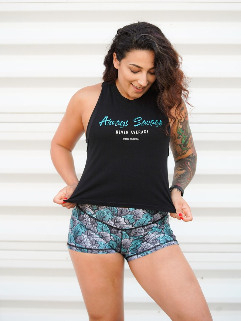 May include: A woman wearing a black tank top with the text "Always Savage Never Average" and blue and gray floral print athletic shorts.