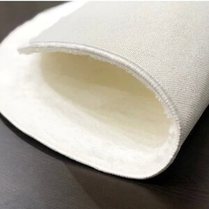 May include: Close-up of a white, round rug with a soft, plush interior. The rug's edge is visible, showing a stitched border. The rug appears to be made of a soft, textured material, suitable for home decor.