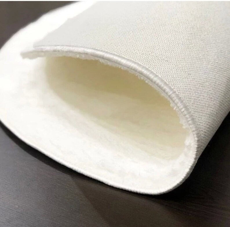 May include: Close-up of a white, round rug with a soft, plush interior. The rug's edge is visible, showing a stitched border. The rug appears to be made of a soft, textured material, suitable for home decor.