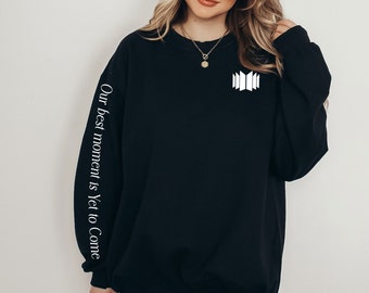May include: Black sweatshirt with white text on the sleeve that reads "Our best moment is Yet to Come" and a white geometric design on the front.
