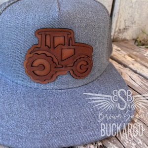 May include: A gray and brown baseball cap with a leather tractor patch. The cap has a mesh back and a curved brim. The text "Brown Sugar Buckaroo" is embroidered on the front of the cap.