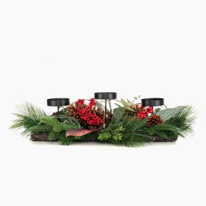 May include: A black metal candle holder with three candle cups, decorated with pine branches, red berries, and pine cones.