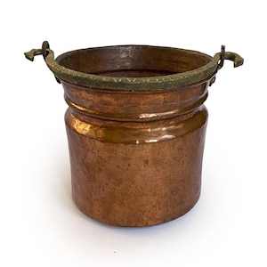 May include: A small copper bucket with a brass rim and two brass handles. The bucket has a hammered finish and is ideal for a rustic or farmhouse decor.