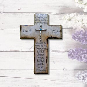 May include: A rustic wooden cross with a distressed white finish. The cross features a silver metal cross with a turquoise stone at the center. The cross is decorated with the text "Isaiah 26:3-4" and the verse "You keep him in perfect peace whose mind is stayed on you because he trusts in you. Trust in the LORD forever, for the LORD GOD is an everlasting..."