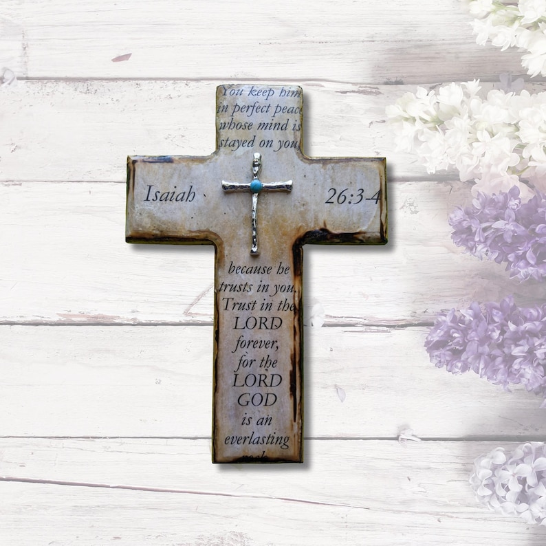 May include: A rustic wooden cross with a distressed white finish. The cross features a silver metal cross with a turquoise stone at the center. The cross is decorated with the text "Isaiah 26:3-4" and the verse "You keep him in perfect peace whose mind is stayed on you because he trusts in you. Trust in the LORD forever, for the LORD GOD is an everlasting..."