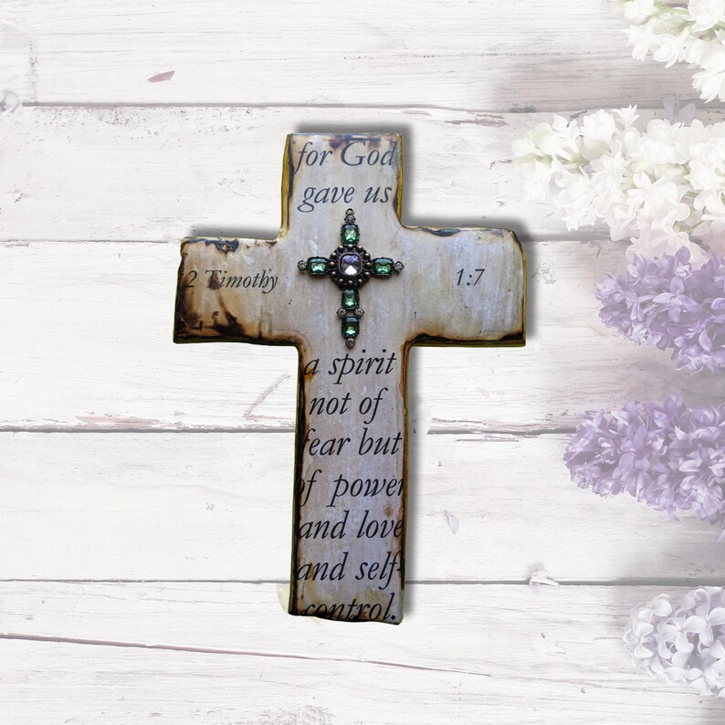 May include: A white wooden cross with a green and purple jeweled center. The cross has the text "2 Timothy 1:7" and the quote "for God gave us a spirit not of fear but of power and love and self control."