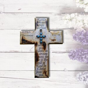 May include: A white wooden cross with a turquoise stone embellishment and the scripture "1 Thessalonians 5:16-18 Rejoice always, pray without ceasing give thanks in all circumstances; for this is the will of God in Christ Jesus for you."