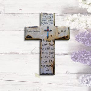 May include: A rustic wooden cross with a distressed white finish and a silver cross charm. The cross features the Bible verse Deuteronomy 31:8, which reads "It is the LORD who goes before you. He will be with you; he will not leave you or forsake you. Do not fear; be not dismayed."