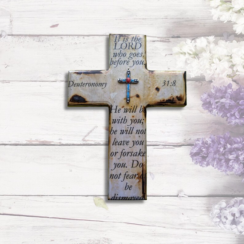 May include: A rustic wooden cross with a distressed white finish and a silver cross charm. The cross features the Bible verse Deuteronomy 31:8, which reads "It is the LORD who goes before you. He will be with you; he will not leave you or forsake you. Do not fear; be not dismayed."