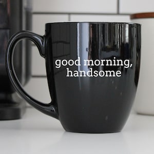 Puede incluir: Taza de café negra con texto blanco que dice "good morning, handsome".