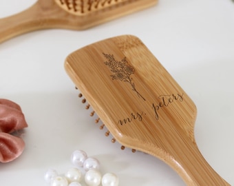 Puede incluir: Un cepillo para el cabello de madera con un diseño floral y el texto "mrs. peters" grabado en el mango.