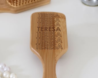 Puede incluir: Un cepillo para el cabello de madera con el nombre "TERESA" grabado varias veces. El cepillo está hecho de bambú natural y tiene un color marrón.