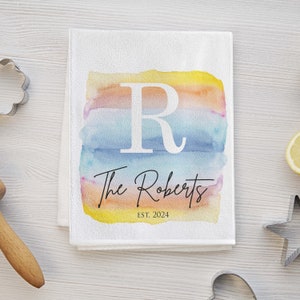 May include: White kitchen towel with a watercolor design in shades of yellow, orange, blue, and pink. The design features a large white letter "R" and the text "The Roberts EST. 2024".