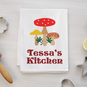 May include: White kitchen towel with a red, yellow, and brown mushroom illustration and the text "Tessa's Kitchen" in red.