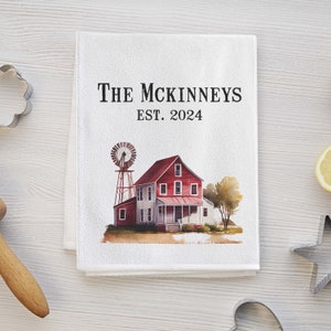 May include: White kitchen towel with a watercolor illustration of a red farmhouse with a windmill, and the text "The McKinneys Est. 2024".
