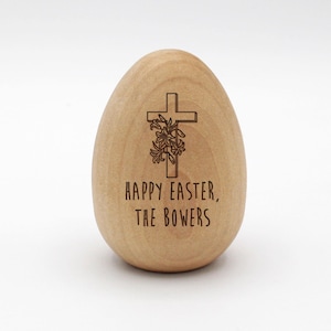 May include: A wooden egg-shaped ornament with a cross and flowers engraved on it. The text "Happy Easter, The Bowers" is also engraved on the ornament.
