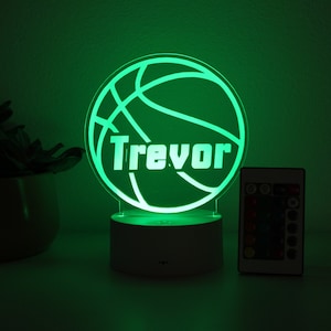 Pu&ograve; includere: Una luce notturna verde a forma di pallone da basket con il nome "Trevor" in bianco. La luce &egrave; su una base bianca, con un telecomando accanto. Il tema &egrave; lo sport e la personalizzazione.