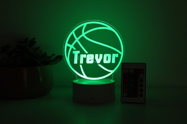 Pu&ograve; includere: Una luce notturna verde a forma di pallone da basket con il nome "Trevor" in bianco. La luce &egrave; su una base bianca, con un telecomando accanto. Il tema &egrave; lo sport e la personalizzazione.