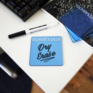 May include: A light blue dry erase board with the text "OLIVER'S DESK Dry Erase" in white and black. A black and white dry erase marker and a black keyboard are also visible.