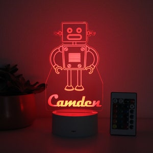 May include: A red LED night light shaped like a robot with the name "Camden" underneath. The light is on a white base and comes with a remote control.