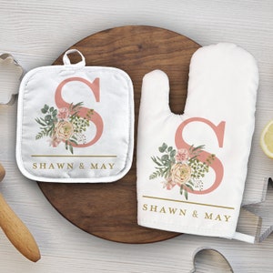 Puede incluir: Un juego de dos accesorios de cocina con un diseño floral con la letra "S" y los nombres "Shawn & May". El juego incluye un posavasos y un guante para horno.