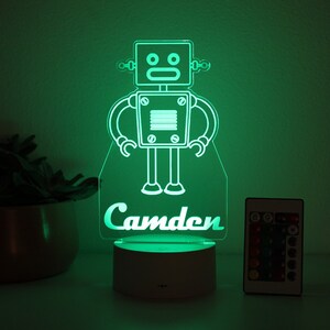 May include: A green LED night light shaped like a robot with the name "Camden" underneath. The light is on a white base and comes with a remote control.