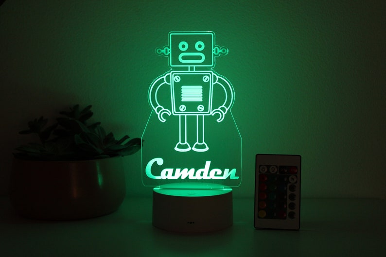 May include: A green LED night light shaped like a robot with the name "Camden" underneath. The light is on a white base and comes with a remote control.