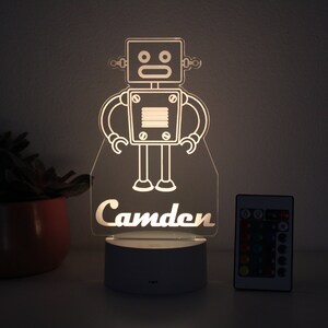 May include: A white robot night light with a remote control. The robot has a square head with two eyes and a mouth. The name "Camden" is written below the robot.