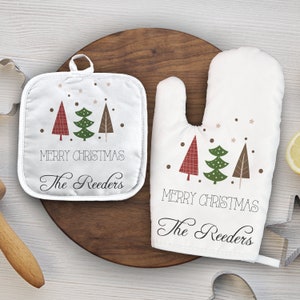 May include: White oven mitts and pot holder with a Christmas tree design. The text "Merry Christmas The Reeders" is printed on both items.